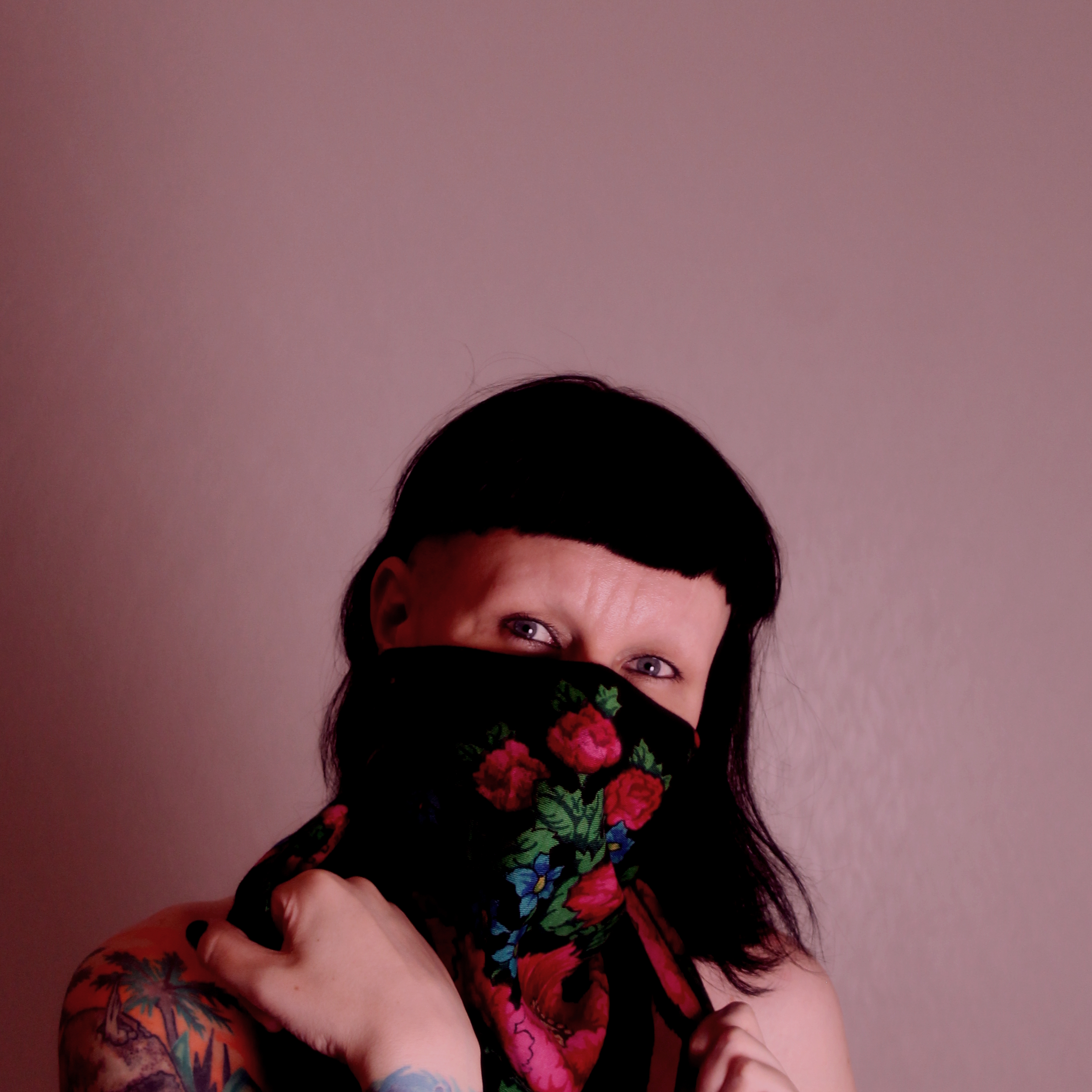 image of Pihla Lehtinen in front of a pink background. Pihla has black hair with a fringe and is wearing a black scarf with red roses on her face.